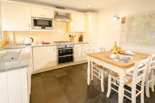 a kitchen with white cabinets and a wooden table at Pippins, Elterwater in Chapel Stile