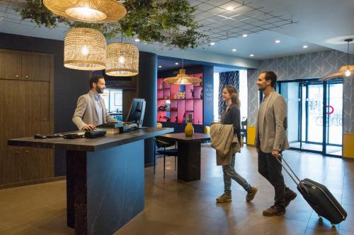 three people in an office with a woman pulling a suitcase at Aparthotel Adagio Annecy Centre in Annecy