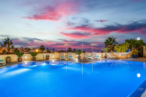 a large blue pool with chairs and a sunset at Haciendas Village Tenerife in Adeje