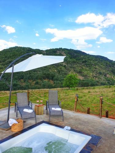 a hot tub with two chairs and an umbrella at The Bubble Valley Piet Retief in Piet Retief
