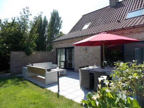 ディクスムイデにあるSun kissed Villa in Diksmuide with Garden Saunaのパティオ(テーブル、赤い傘付)