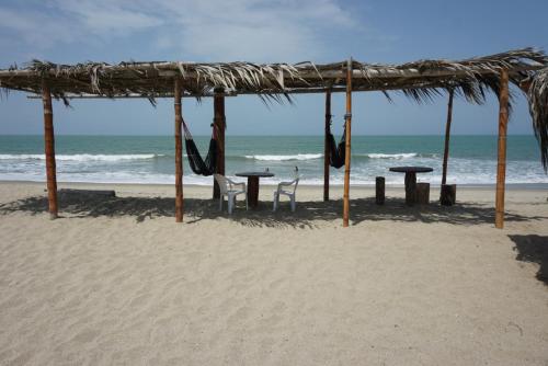 a beach with tables and chairs and a straw umbrella at Hostel Paqaryi in Zorritos