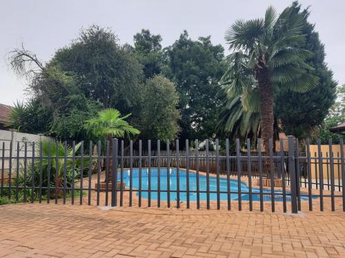 a fence around a swimming pool with a palm tree at Housemartin Guest House in Klerksdorp