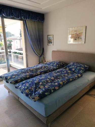 sypialnia z łóżkiem z niebieskimi prześcieradłami i oknem w obiekcie Condominio Golfo d'Oro w mieście Ascona