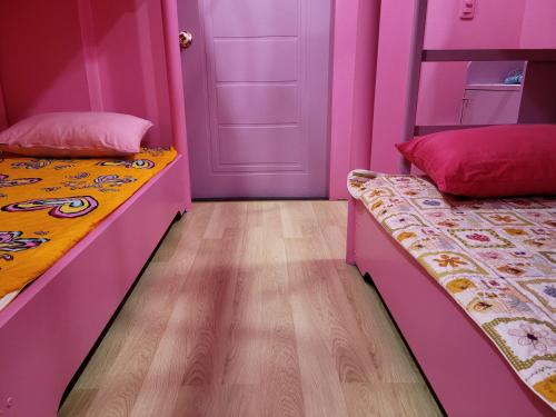 two beds in a room with pink walls and wooden floors at Jeju Vision House in Jeju