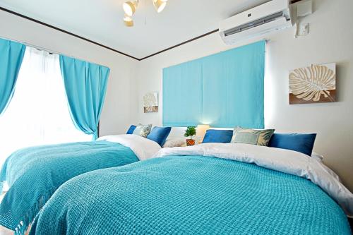 two beds in a room with blue curtains at ゲストハウスえらぶ〜 in Wadomari