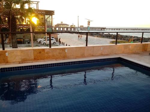 a swimming pool next to a beach with a pier at Tabajara Flats Praia de Iracema in Fortaleza