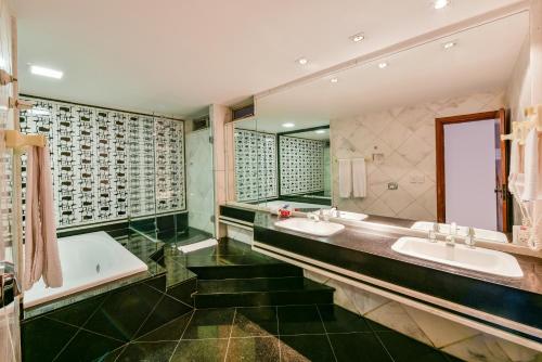 baño con 2 lavabos, bañera y espejos en Plaza Inn Augustus en Goiânia