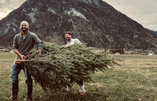 two men are holding a large pile of grass at Forest Chalet, 15 min to salzburg olt town, and most beautiful lakes, secluded location, 1,000 sqm garden, mountainview, panorama sauna, bath whirlpool, BBQ&bikes&sunbeds for free, up to 10 p in Golling an der Salzach