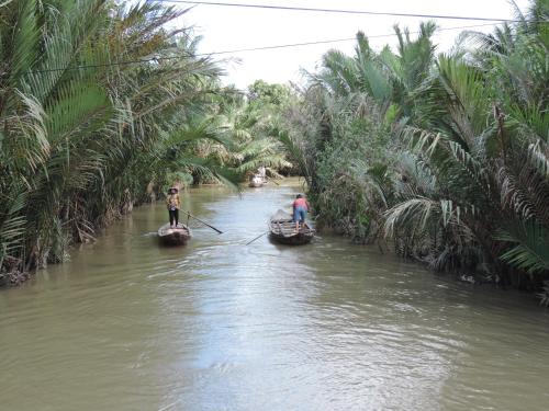 two people on boats in a river with palm trees at Ben Tre Farm Stay in Ben Tre
