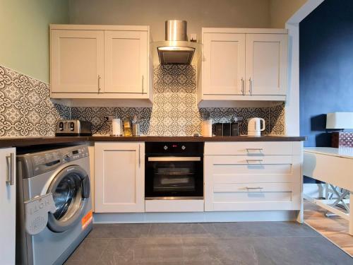 a kitchen with white cabinets and a washer and dryer at The Edinburgh Victorian - 3 Bedroom Apartment in Edinburgh