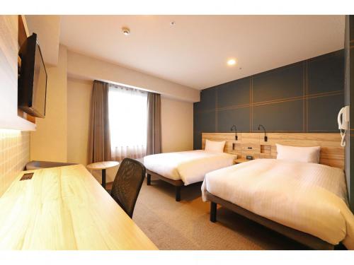 藤沢市にあるスマイルホテル湘南藤沢のベッド2台とテーブルが備わるホテルルームです。