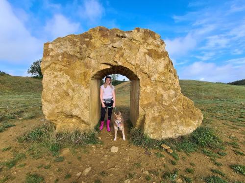 a woman and a dog standing next to a rock at Shepherds Huts Ham Hill, 2 double beds, Bathroom, Lounge, Diner, Kitchen, LOVE dogs & Cats Looking out to lake and by Ham Hill Country Park plus parking for large vehicles available also great deals on workers long term This is the place to relax and BBQ in Yeovil