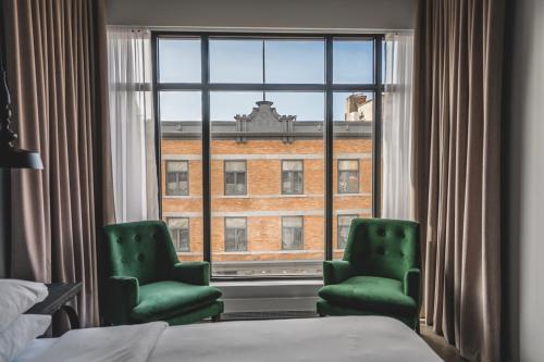 トロワ・リヴィエールにあるHotel Oui GO!の緑の椅子2脚と窓が備わるホテルルームです。