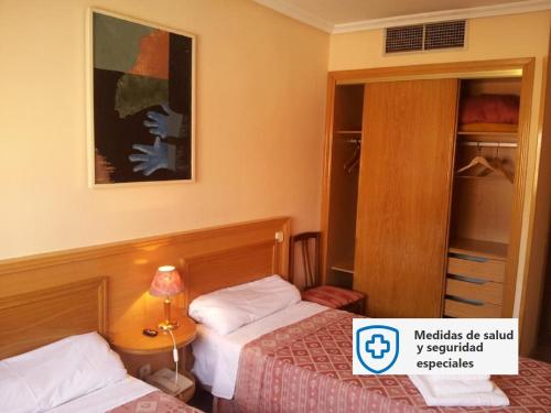 una camera d'albergo con due letti e uno specchio di Hostal Juan XXIII a San Sebastián de los Reyes