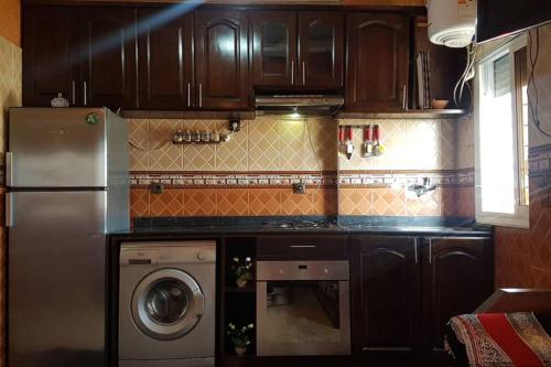 cocina con armarios de madera, lavadora y secadora en un logment limineux toute la journé confortable, en Sale