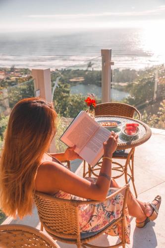 Eine Frau, die an einem Tisch sitzt und ein Buch liest. in der Unterkunft Pousada Caminho do Rei in Praia do Rosa