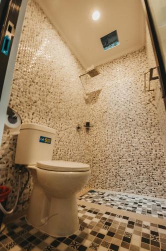 a bathroom with a toilet and a tiled wall at Dados Guest House in Canggu