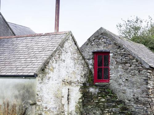um antigo edifício de pedra com uma janela vermelha em Lake House em Dunmanway
