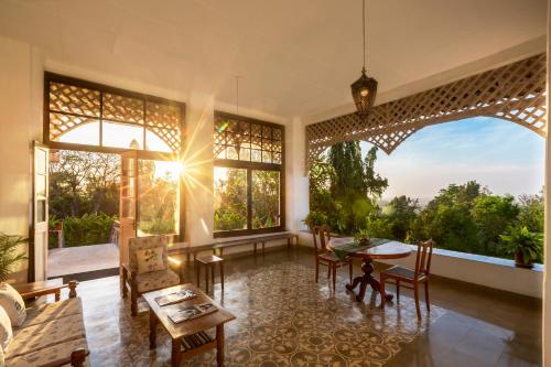 een woonkamer met een tafel en stoelen en grote ramen bij Ama Plantation Trails Coorg in Gonikoppal