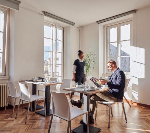 a man sitting at a table in a room with windows at Lainez Rooms & Suites in Trento