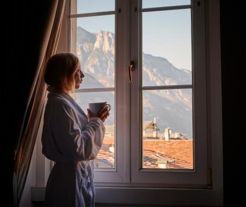 a woman standing in front of a window holding a cup at Lainez Rooms & Suites in Trento