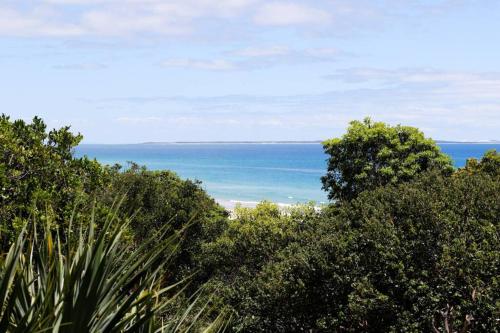 a view of the ocean from behind some trees at Waves 8 - Beachfront with pool in Point Lookout