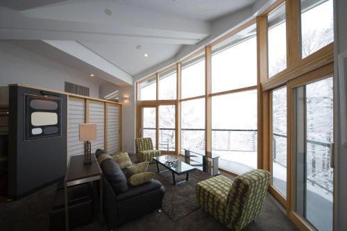 a living room with a couch and chairs and windows at The Ridge Hakuba Hotel & Apartments in Hakuba