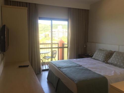 1 dormitorio con 1 cama y balcón con vistas. en Studio em Jurerê em hotel a beira-mar, en Florianópolis