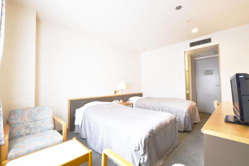 a room with two beds and a chair and a tv at Nayoro Onsen Sunpillar in Nayoro