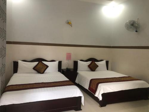 um quarto com 2 camas com lençóis brancos e almofadas castanhas em Mai Vuong Thuy Hotel em Thu Dau Mot