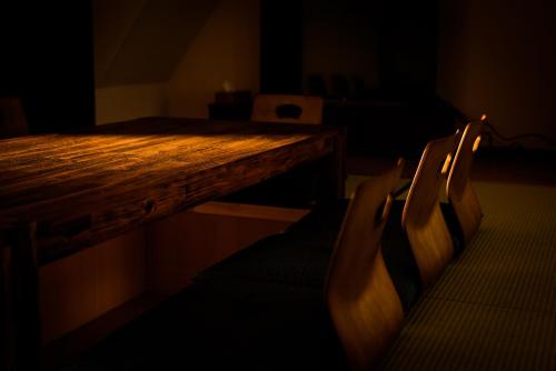 Biker's Inn Onomichi 自転車の宿おのみち في أونوميتشي: طاولة وكراسي خشبية في غرفة مظلمة