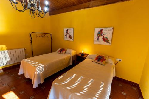 two beds in a room with yellow walls at Casa Rural El Abeto in Torre de Don Miguel