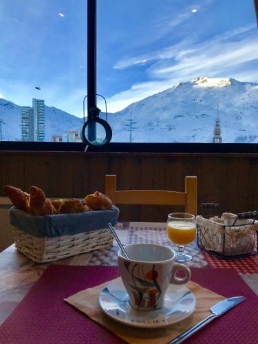 a table with a cup of coffee and a basket of bread at Hotel Le Pelvoux in Les Menuires