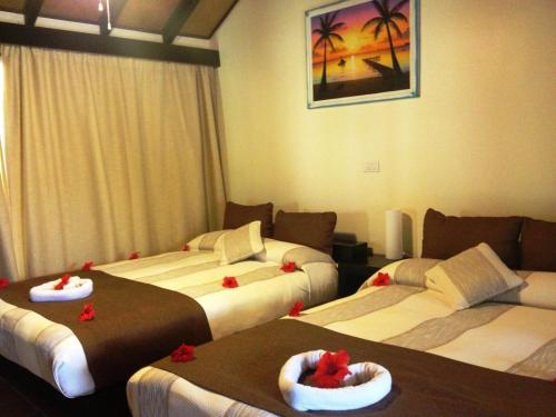 Media Luna Resort & Spa في First Bight: غرفة فندقية بثلاث اسرة عليها بعرصي حمراء