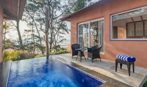 a swimming pool with chairs and a table next to a house at Mandrem Beach Resort, a member of Radisson Individuals Retreat in Mandrem