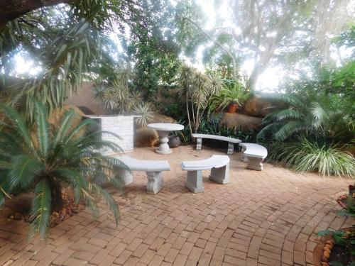un patio con bancos, árboles y palmeras en Fouriestreet 199 Bed and Breakfast en Mokopane