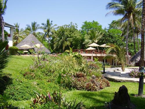 a garden with tables and umbrellas in a resort at Pinewood Beach Resort and Spa in Diani Beach