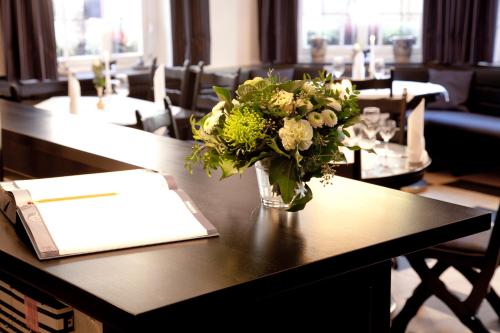 a vase of flowers on a table with a book at Hotel Restaurant Telgter Hof in Telgte