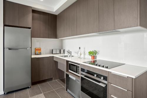 a kitchen with wooden cabinets and a stainless steel refrigerator at Quest Preston in Melbourne