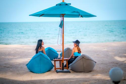 dos mujeres sentadas bajo un paraguas en la playa en Khanom Sea Beach Resort, en Nakhon Si Thammarat