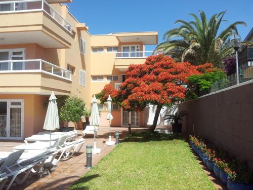 a building with chairs and a tree with red flowers at Apartamentos Horizonte in Playa del Ingles