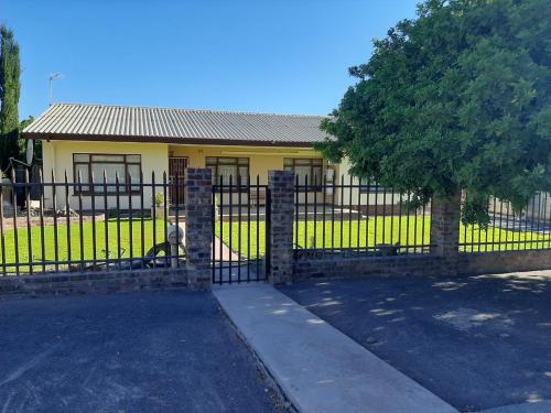 a fence in front of a house with a dog behind it at Dagbreek in Beaufort West