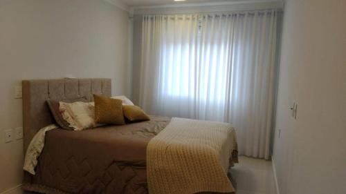 a bedroom with a bed and a window with curtains at Apto a uma quadra do mar em torres in Torres