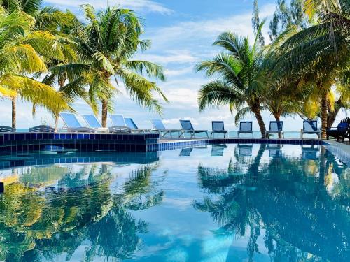 a swimming pool with palm trees and lounge chairs at Maya Beach Hotel in Maya Beach