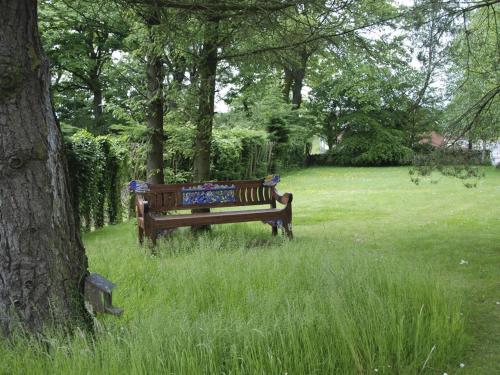 un banco del parque sentado en el césped junto a un árbol en Armidale Cottages B&B, en Workington