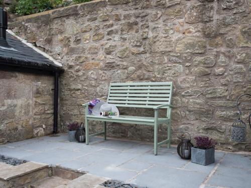 a green bench sitting in front of a stone wall at Chatton Cottage in Chatton