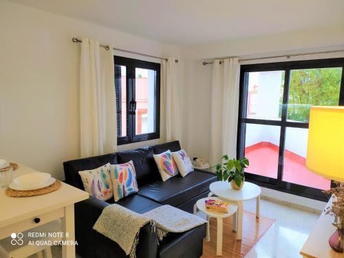 Una sala de estar con un sofá negro y una ventana. en Ático Galileo, en La Línea de la Concepción