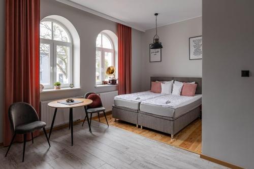a bedroom with a bed and a table and two windows at Apartamenty Kamienica in Sieradz