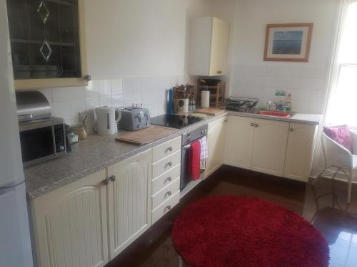 a kitchen with white cabinets and a red rug at Spacious Victorian Flat 3 bed, Ideal Base for Snowdonia in Bangor